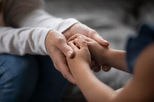 compassionate young foster parent holding hands of little kid girl