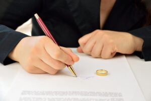 wife signing divorce agreement with the weeding ring on the contract